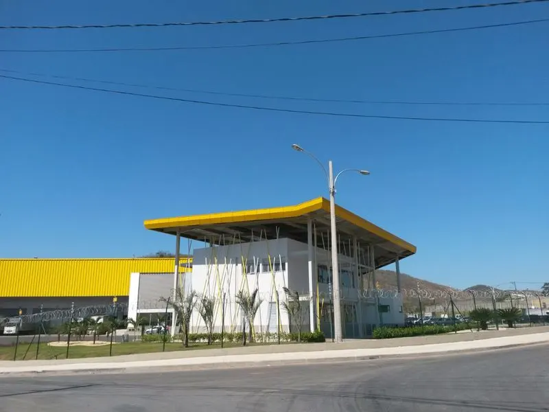 Vista a partir da rua do CD Casa e Vídeo, em Queimados/RJ: edifício de apoio com cobertura amarela e galpão ao fundo.