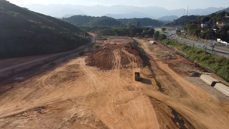 CD King Ouro em Duque de Caxias/RJ: terraplenagem com caminhões e escavadeiras, rodovia e serra ao fundo