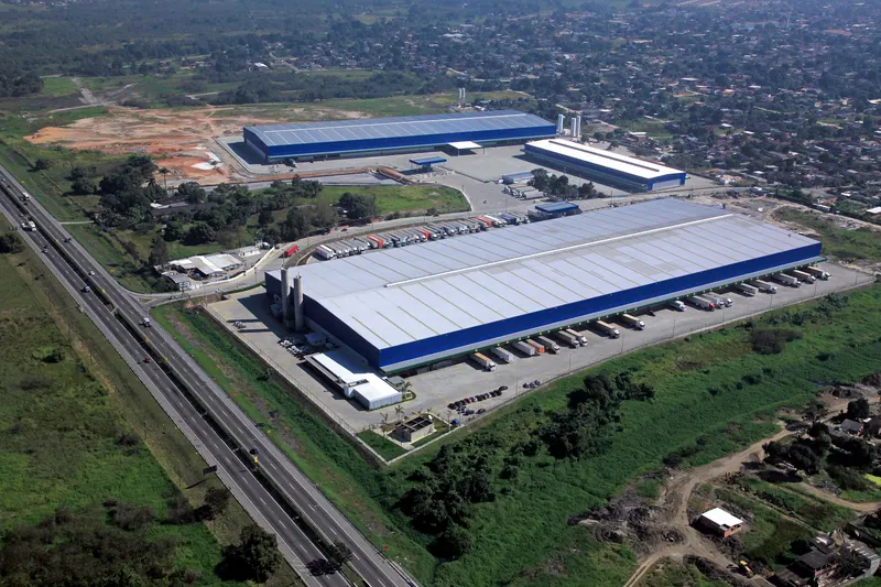Vista aérea do complexo do CD L'Oréal, em Duque de Caxias/RJ, com galpões, docas e a rodovia ao lado.