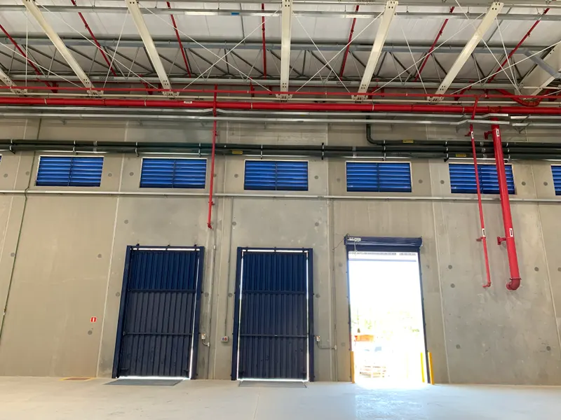 Interior do galpão do Condomínio Logístico BZLog, em Duque de Caxias/RJ: estrutura metálica da cobertura, rede de sprinklers e portões.